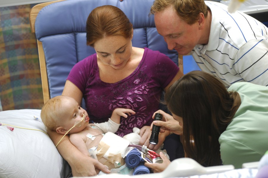 Dana Nichols, R.N., checks the ventricular assist device implanted in infant Nathan Roberts, here with his parents, Amanda and James. (photo by Anne Rayner)