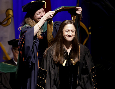 Anna Whitney smiles while receiving her VUSM academic hood from Amy Fleming, MD, MScHPE.