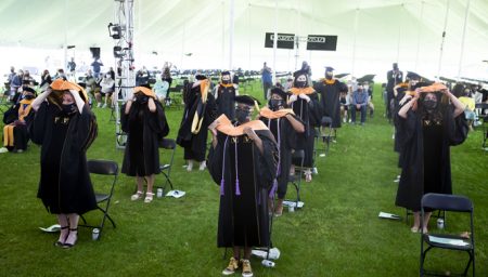 Graduates stand and don their academic hoods in a ceremonial group hooding. 