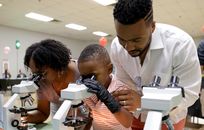 Sage Davis, 4, observes microbial “snakes” and “space bears” (tardigrades) under the microscope with his parents, Corinne and Gerald.