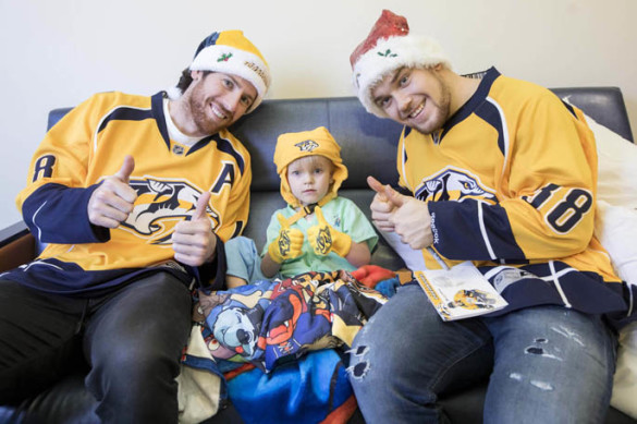 Players from the Nashville Predators hockey team brought some holiday cheer and Kids Club gift packs during a recent visit to patients at Monroe Carell Jr. Children’s Hospital at Vanderbilt. Players stopped by Seacrest Studios to play a game and then visited with patients unable to leave their rooms. Here, James Neal, left, patient Caleb Aslinger, 3, and Viktor Arvidsson, give a thumbs up to some of the gear inside the Kids Club pack. (photo by John Russell)