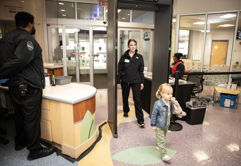 VUPD Community Service Officer Samuel M. Burrell looks on as Billie Parks and her mother, Anna Parks, pass through one of the new weapons detection installations at Monroe Carell Jr. Children’s Hospital at Vanderbilt. (photo by Erin O. Smith)
