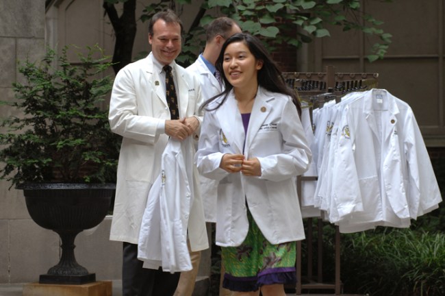 Jeff Balser, M.D., Ph.D., looks on as Tyffany Chen tries on her white coat. (photo by Anne Rayner)