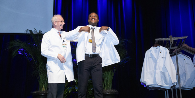 Donald Brady, MD, left, helps helps Godwin Emeka put on his white coat. (all photos by Susan Urmy)