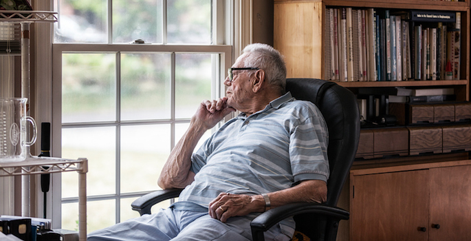 elderly man lost in thought and looking out window in home office