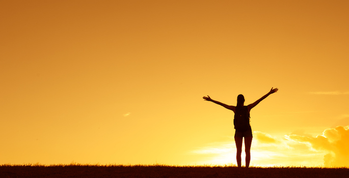 Silhouette of woman with arms raised joyfully against the sunset
