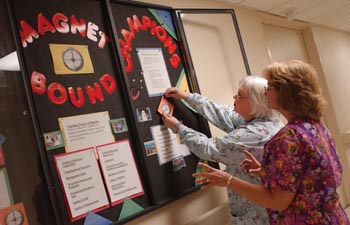 Elaine Atteberry and Deb Rassel, nurses and Magnet Champions in Radiology, work together on the bulletin board informing the department’s staff about the Magnet program. 
Photo by Dana Johnson