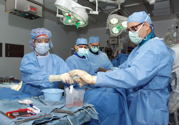 Instead of opening a patient's chest, Tom Naslund, M.D., right, and scrub nurse Beth Spallinger, R.N., thread the new graft into the thoracic aorta on a thin wire through a small incision in the groin. Jim Bob Faulk, M.D., and Raul Guzman, M.D., assist.
photo by Anne Rayner