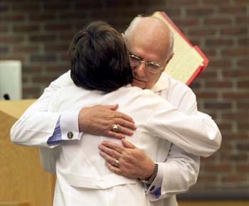 Dr. Deborah German hugs Dean John Chapman after presenting him with a special gift, a traditional white coat embroidered with the name “Dean of Deans.” (photo by Dana Johnson)