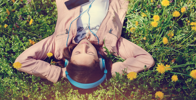 serene girl lying in a meadow listening to music on headphones