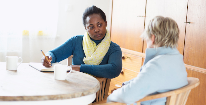 social worker listening to a client, sitting at table and taking notes